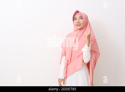 Ein Porträt einer glücklichen asiatischen muslimischen Frau, die einen Schleier oder Hijab trägt, der auf sie zeigt oder etwas über ihr präsentiert. Isoliert auf weißem Hintergrund mit Kopierrac Stockfoto