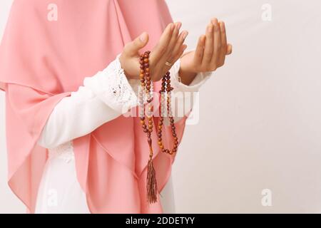 Ein Porträt einer asiatischen muslimischen Frau, die einen Schleier oder Hijab trägt und mit Gebetsperlen auf der Hand betet. Nahaufnahme. Isoliert auf weißem Hintergrund mit Kopie Stockfoto