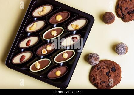 Schachtel Pralinen mit Nüssen und Schokoladenkeksen auf gelbem Hintergrund. Blick von oben. Stockfoto