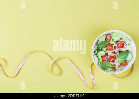 Gesunde ausgewogene Ernährung Konzept, Salat mit Gurken Tomate Zwiebel Salatblätter mit Maßband auf gelbem Hintergrund. Draufsicht copy space Stockfoto