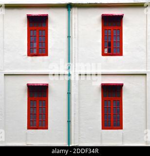 Ein restauriertes altes Gebäude mit vier leuchtend roten Fensterrahmen an einer weißen Steinmauer. Stockfoto