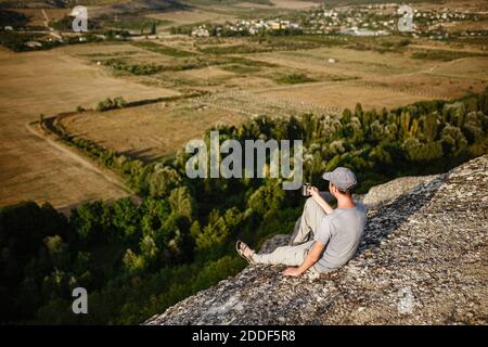 Rückansicht eines jungen Mannes, der Tee oder Kaffee in den Bergen trinkt. Reisender Mann mit Bart hält in den Händen eine Tasse Tee, nach dem Wandern. Reisen, Lifestyle, VA Stockfoto