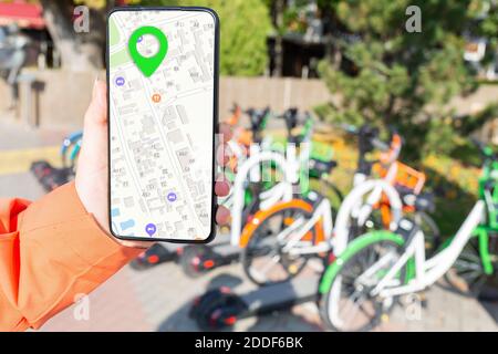 Die Hand der Frau hält ein Smartphone und zeigt eine App mit einer Online-Karte. Ein Fahrradparkplatz ist im Hintergrund. Konzept der modernen Technologien und re Stockfoto