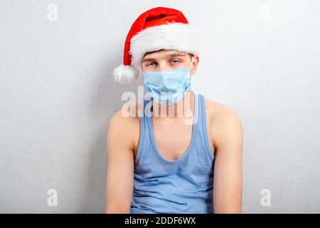 Trauriger junger Mann in Weihnachtsmütze und Grippe Maske von Die Wand im Raum Stockfoto