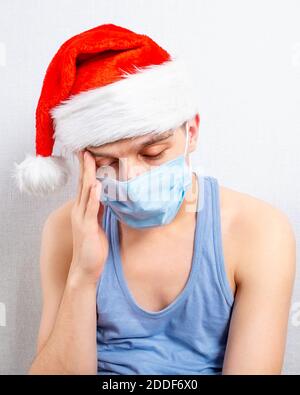 Trauriger junger Mann in Weihnachtsmütze und Grippe Maske von Die Wand im Raum Stockfoto