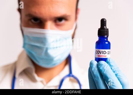 Junge männliche Arzt hält covid-19 Impfstoff blaue Fläschchen. Konzept der Wissenschaft und Corona-Virus-Impfstoff. Gesichtsmaske und Stethoskop auf weißem Hintergrund. Stockfoto