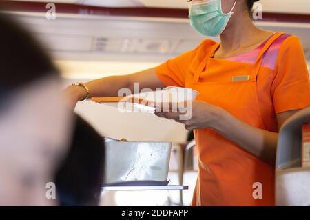 Flugbegleiter in Gesichtsmaske Schutz von covid-19 serviert Passagiere ein Getränk. Stockfoto