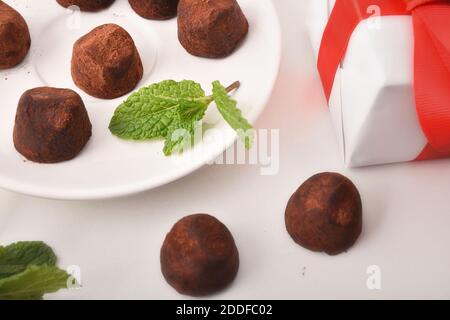 Schokoladentrüffel auf weißem Tisch mit Geschenk. Ansicht von oben. Horizontale Zusammensetzung. Stockfoto