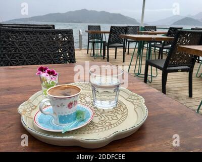 Traditionelle Präsentation von türkischem Kaffee in Keramik-Tasse und Vintage-Tablett mit türkischen Delight, Glas Wasser und rosa frischen Blumen. Garten im Freien Stockfoto
