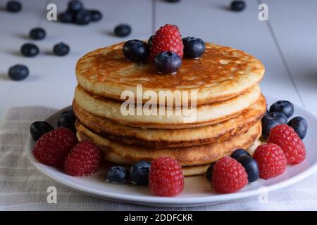 Teller Pfannkuchen mit Ahornsirup, Heidelbeeren und Himbeeren auf weißem Holztisch. Stockfoto