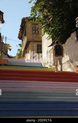 Mann mit Rucksack Klettern bunt bemalten Treppen. Regenbogenfarben bemalte Treppe Straße. Altes Haus und Mauer. Stockfoto