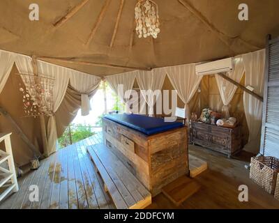 Blaues komfortables Massagebett im beigefarbenen Sommerzelt mit weißen Vorhängen und Meerblick im Freien. Entspannende exotische Luxus Sommerurlaub Therapie im Freien. Stockfoto