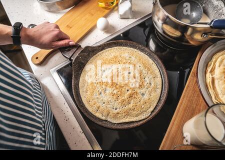 Frau steht am Herd und frittiert Pfannkuchen in einer heißen Pfanne. Konzept des Prozesses der Herstellung eines leckeren Frühstück zu Hause. Stockfoto