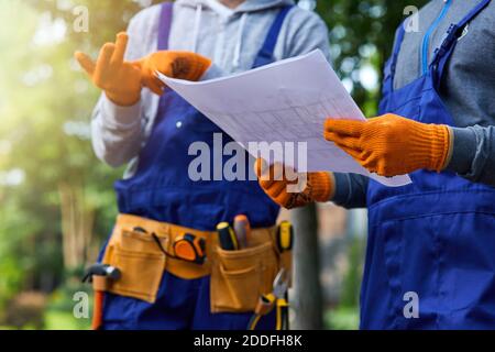 Nahaufnahme von zwei Bauherren, die draußen mit einem offenen Bauplan stehen, der den Bau der Hütte diskutiert. Aufbau, Teamarbeit, Partnerschaftskonzept Stockfoto