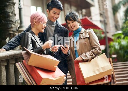 Drei junge asiatische modische Menschen navigieren mit Handy beim Einkaufen In der Stadt Stockfoto