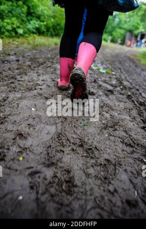 Geringe Schärfentiefe (selektiver Fokus) mit einer jungen Dame in rosa Gummistiefeln auf einer schlammigen unbefestigten Straße bei einem Musikfestival. Stockfoto