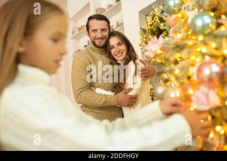 Papa setzen Bälle auf weihnachtsbaum, während seine Frau und Tochter beobachtet ihn Stockfoto