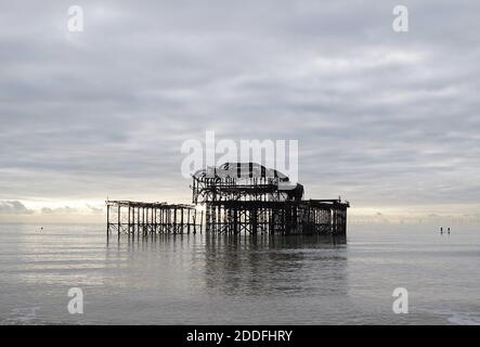 Die verbrannte Ruine des West Pier, Brighton, East Sussex, in EINEM ruhigen Meer mit zwei Paddle Boarders und Rampion Wind Farm Stockfoto