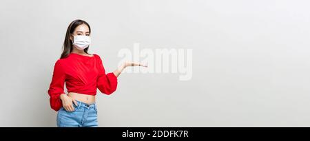 Asiatische Frau trägt medizinische Maske und offene Hand zu leeren Platz beiseite auf hellgrauem Studio-Banner-Hintergrund mit Kopie Platz Stockfoto