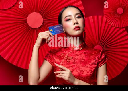 Portrait der schönen asiatischen Frau trägt traditionelle Cheongsam Qipao Kleid Zeigt Kreditkarte in der Hand auf rotem orientalischem Hintergrund für Chinesisch neu ja Stockfoto