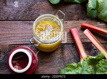 Hausgemachte Bio-Rhabarbermarmelade in einem Glas und frisch Rhabarber Stiele auf einem dunklen alten Holztisch Stockfoto