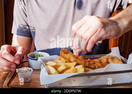Man's Hand bestreut mit Zitronenfisch und Chips Stockfoto