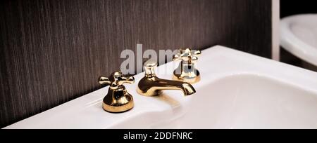 Weißes und sauberes Waschbecken mit einem goldenen Wasserhahn. Vintage Bad Wasserhahn, Hotel Innenarchitektur. Klare und minimalistische Aufnahme mit dunklem Hintergrund. Stockfoto