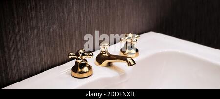 Weißes und sauberes Waschbecken mit einem goldenen Wasserhahn. Vintage Bad Wasserhahn, Hotel Innenarchitektur. Klare und minimalistische Aufnahme mit dunklem Hintergrund. Stockfoto