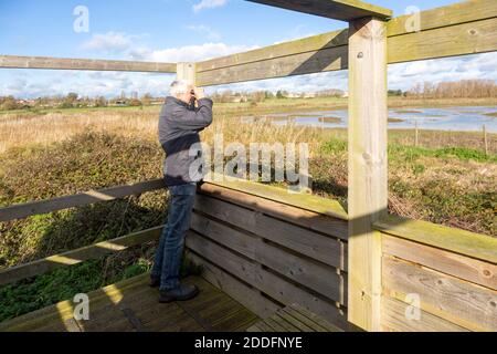 Männliche Vogelbeobachter Ornithologe mit Fernglas verstecken sich bei RSPB Hollesley Marshes, Suffolk, England, UK Stockfoto