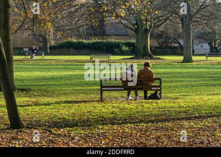 Junges Paar sitzt auf einer Parkbank genießen die Wintersonne, Abington Park, Northampton, Großbritannien Stockfoto