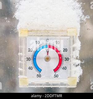 Thermometer in Form einer Uhr vor dem Fenster Mit einer Schneekappe Stockfoto