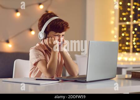 Unzufriedener Junge mit Kopfhörern, der sitzt und sich die Lektion oder den Kurs ansieht Online auf dem Laptop zu Hause Stockfoto