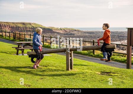 Ein junger Bruder und eine Schwester spielen auf einer Wippe in einem Park in Crail, Fife, Schottland. Dieser Park liegt am Küstenweg und ist in einer sehr schönen Lage Stockfoto