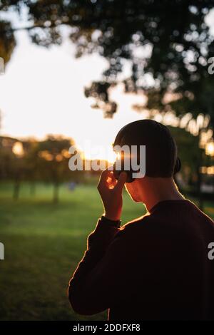 Blonde kaukasischen Jungen Musik hören mit kabellosen Kopfhörern bei Sonnenuntergang, trägt einen roten Pullover. Konzept der Technik. Musik auf der Straße. Stockfoto