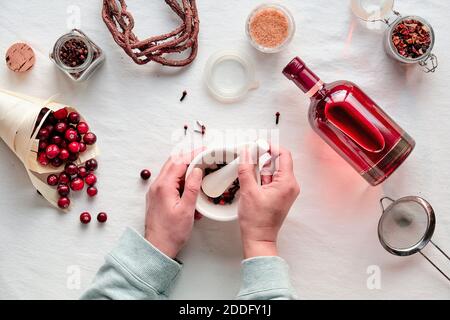 Hausgemachter Alkohole-Drink. Preiselbeertinktur mit Beeren, Hände zerdrücken Gewürze in Mörser flach legen Stockfoto