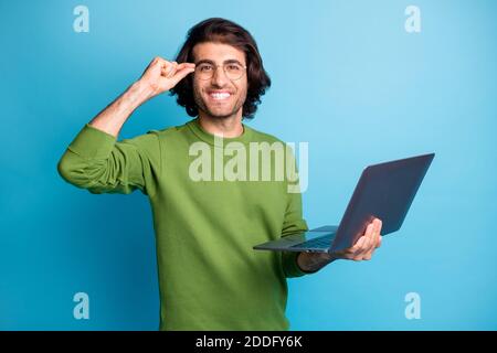 Foto von positiven bärtigen Kerl halten Laptop toothy Lächeln Finger Specs tragen grünen Pullover isoliert blaue Farbe Hintergrund Stockfoto