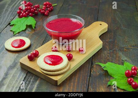 Viburnum Marmelade mit Cookies auf Holzbrett mit Ästen, Blätter verziert. Herbstkomposition. Konzept des Frühstücks Stockfoto