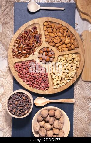 Auswahl an Nüssen Erdnüsse, Haselnüsse, Mandeln, Cashewkerne, Walnüsse, Pekannüsse auf einem Holztisch. Vertikales Foto von oben Stockfoto