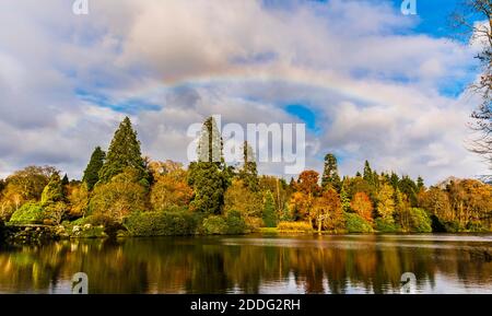 Regenbogen und Herbstfarben über dem See im Sheffield Park, Sussex, Großbritannien Stockfoto