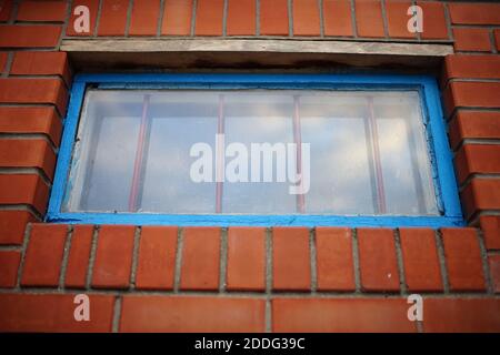 Niedriges Fenster mit blauem Rahmen und Eisengitter in einem Ziegelgebäude Stockfoto