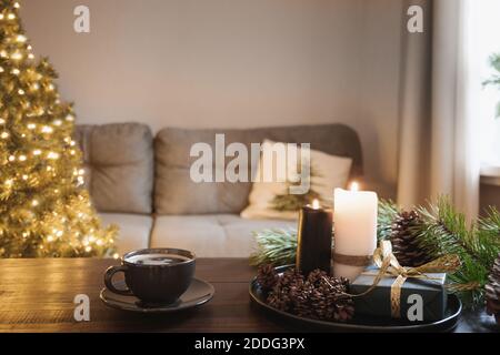 Gemütliches Interieur mit Weihnachtsbaum und warme Tasse Kaffee auf Holz-Tischplatte mit Kerzen, Geschenke Kegel im Wohnzimmer. Weihnachten Urlaub zu Hause. Stockfoto