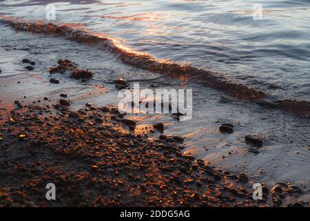 Kiesstrand in der Nähe mit Surfen Meer in einem Sonnenuntergang Licht. Steine in verschiedenen Größen auf dem Hintergrund des Meeres in Abenduntergang. Stockfoto