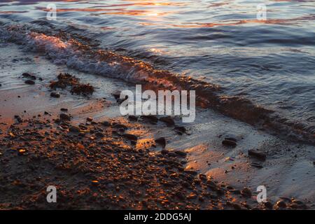 Kiesstrand in der Nähe mit Surfen Meer in einem Sonnenuntergang Licht. Steine in verschiedenen Größen auf dem Hintergrund des Meeres in Abenduntergang. Stockfoto