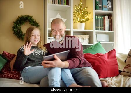 Vater und seine Tochter mit Online-Videoanruf auf Weihnachtszeit. Plaudern mit entfernter Familie während der Pandemie. Während der Winterferien sicher bleiben. Stockfoto