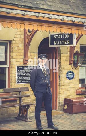 Bahnhofsmeister in Uniform lächelt direkt vor der Kamera, isoliert im Dienst an einer britischen Dampfeisenbahnstation. Stockfoto