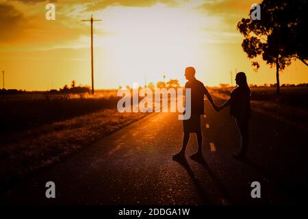 Die Silhouetten eines Paares, das sich die Hände hält Bei Sonnenuntergang unterwegs Stockfoto
