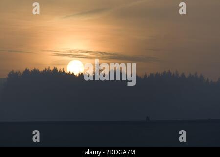 Drei Personen und ein Hund gehen an der Spitze einer Staumauer an den Redmires Stauseen in der Nähe von sheffield entlang. Hinter ihnen ein trüber goldener Sonnenuntergang Silhouetten ein Wald Stockfoto