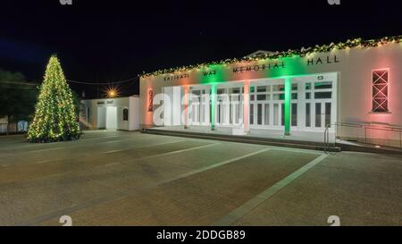 Die war Memorial Hall in Katikati, Neuseeland, beleuchtet in der Nacht mit grünen und roten Weihnachtsbeleuchtung. Ein Weihnachtsbaum steht auf dem Platz vor der Tür Stockfoto
