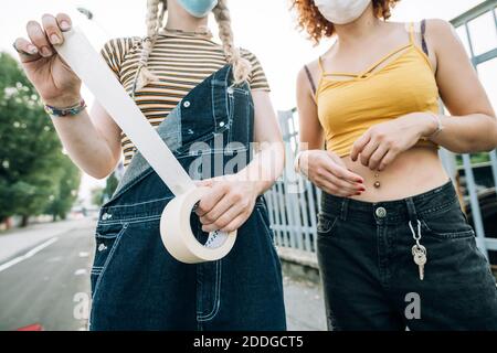 Junge Frauen tragen Masken und halten eine Rolle Klebeband Stockfoto