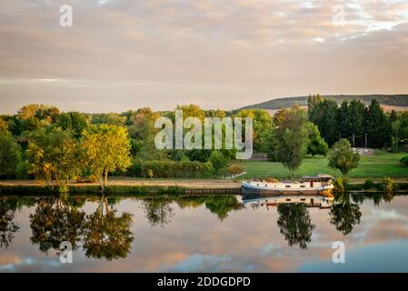 Boot auf dem Fluss Yonne mit Reflexionen bei Sonnenuntergang bei Joigny in Burgund, Frankreich. Stockfoto